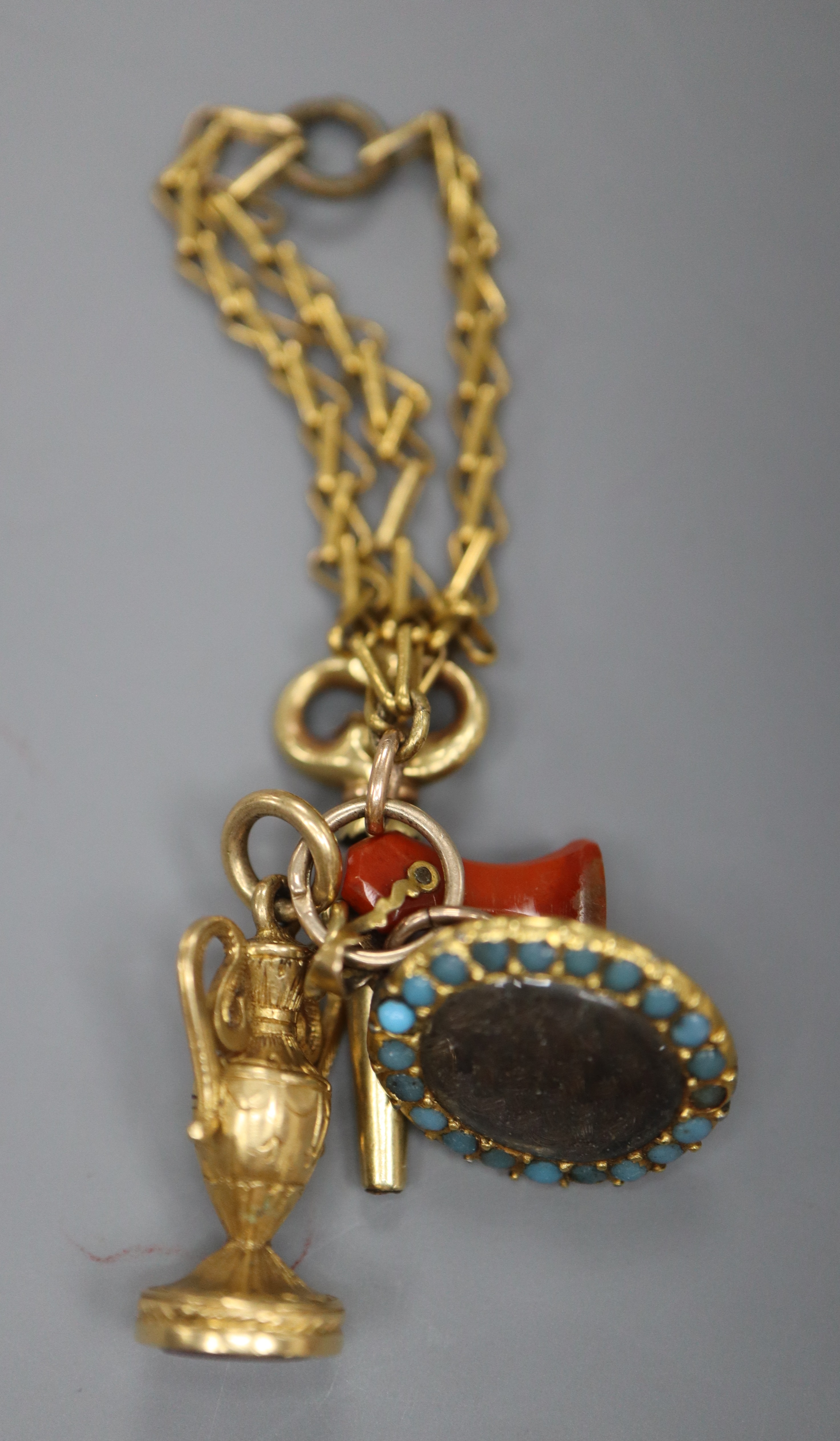 A group of four assorted charms on a yellow metal small chain, including a watch key and carnelian seal.